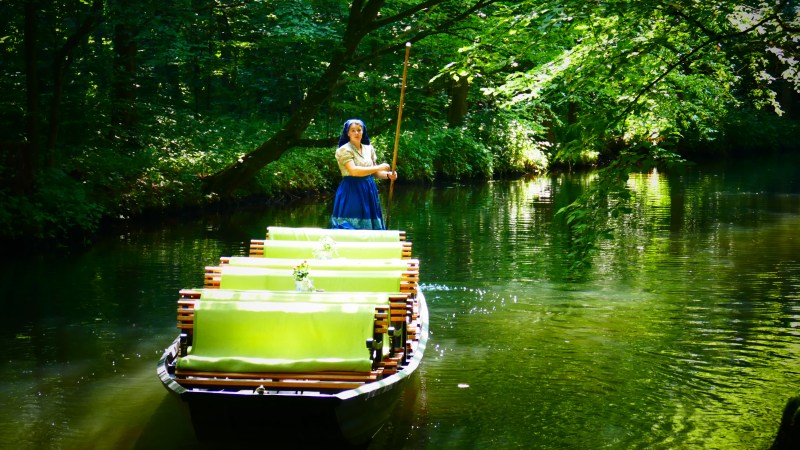 Foto von Fährfrau Yvonne auf Ihren Kahn auf dem Fluss. Die Sitzbänke die mit hellgrünen Sitzbezügen überzogen sind